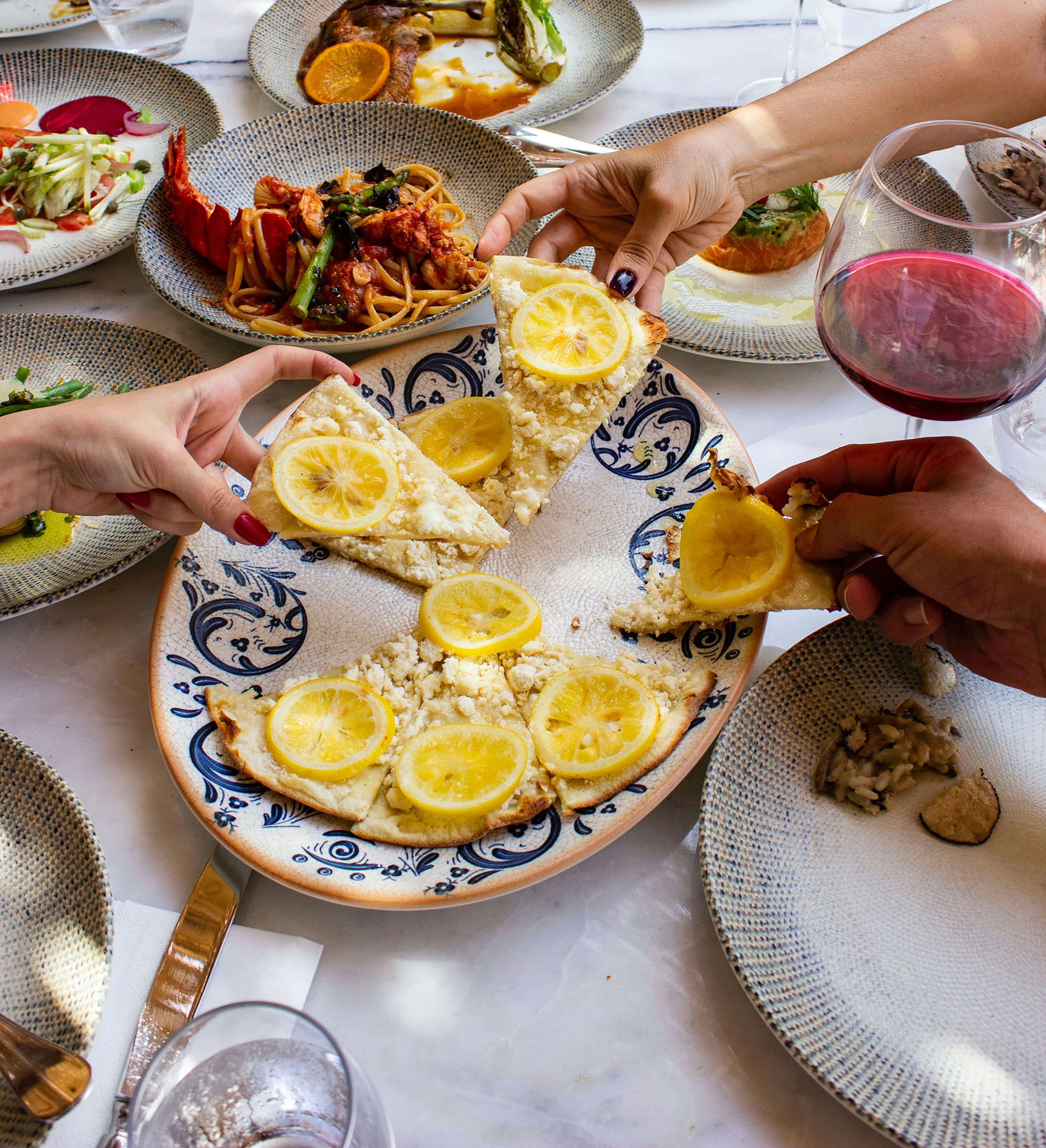 Two pairs of hands passing food across a dinner table.